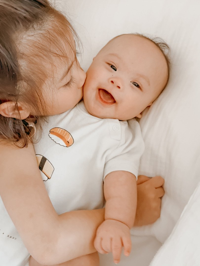 Olli smiling as an older sibling kisses his cheek